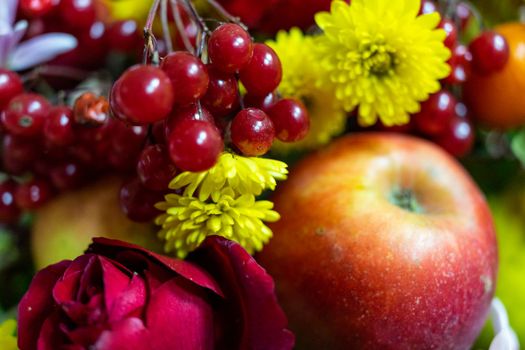 Still life consisting of apples, red viburnum, and yellow flowers close-up.