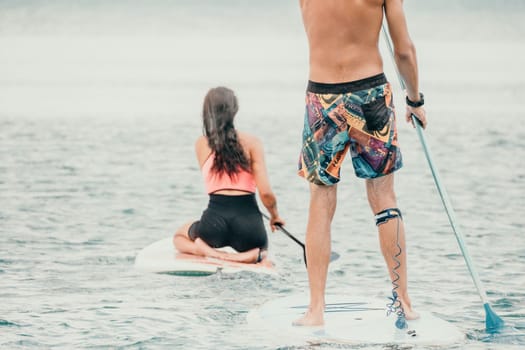 Sea woman and man on sup. Silhouette of happy young woman and man, surfing on SUP board, confident paddling through water surface. Idyllic sunset. Active lifestyle at sea or river