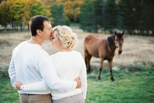 Man kisses woman on the forehead hugging her. Back view. High quality photo