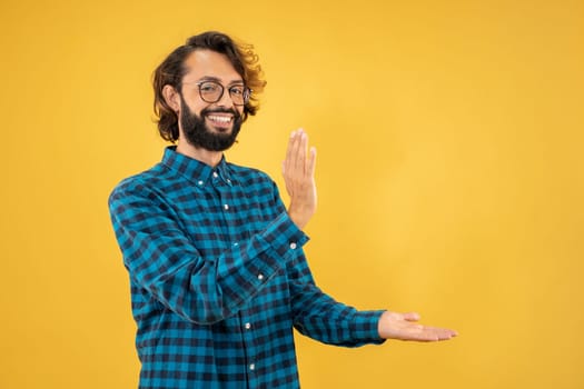 Young man standing over isolated yellow background pointing aside with hands open palms showing copy space, presenting advertisement smiling excited happy. High quality photo