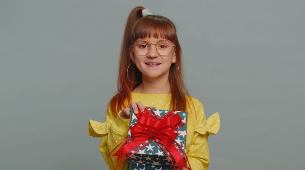 Happy toddler school girl receive, opening gift box and smiling joyfully, looking amazed satisfied with nice present unexpected birthday surprise. Teen female child kid isolated on gray background