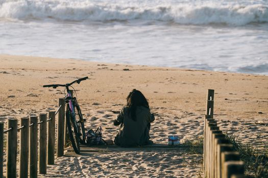 Girl alone with a bicycle sitting on the beach relaxed and calm in front of sea waves