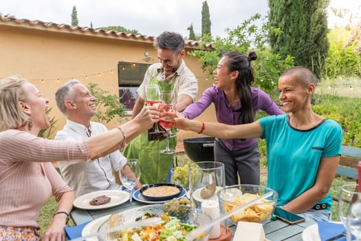 Group of cheerful middle-age friends toasting with beautiful smile around the table at house patio diner. High quality photo