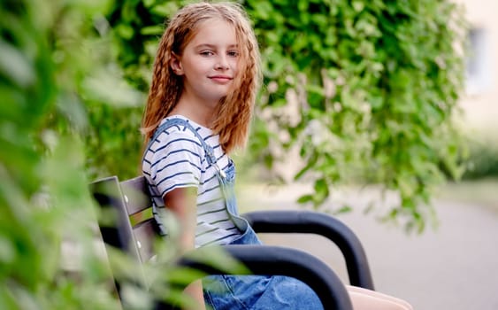 Beautiful preteen girl in city in summertime closeup portrait. Pretty female kid looking at camera in sunny day with blurred background