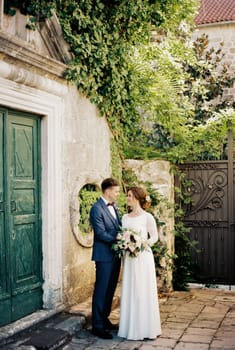 Groom and bride with a bouquet are standing in the garden near the old building. High quality photo