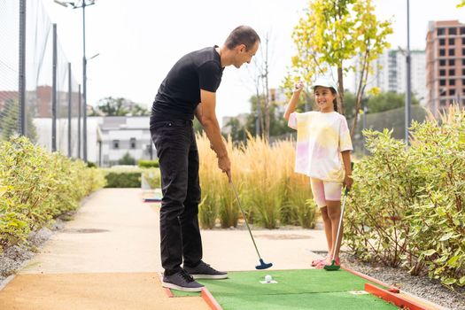 Family playing miniature golf outdoors.