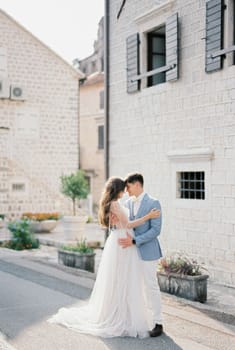 Groom hugs bride near the white facade of an ancient building. High quality photo