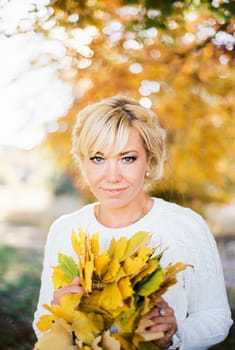 Smiling woman holding a bouquet of yellow leaves in her hands. Portrait. High quality photo