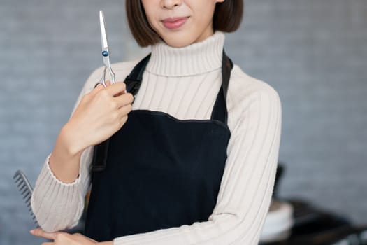 Portrait of a young asian female hairdresser holding qualified haircut tools in her salon for a woman's haircut. Photo job concept for small business owner and haircare.