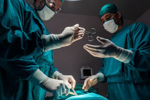 Surgical team performing surgery to patient in sterile operating room. In a surgery room lit by a lamp, a professional and confident surgical team provides medical care to an unconscious patient.