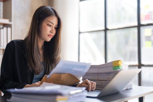 Concentrated young beautiful businesswoman working on laptop and in have documents on hand at bright modern office.