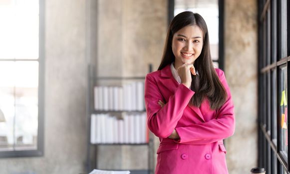 Smiling woman at her desk in office. Happy business woman in office with fingers touching her chin.