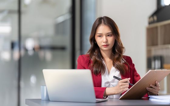 Young Asian businesswoman sitting at their desk and take notes using laptop in the office.