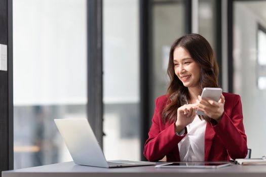 business woman holding smartphone getting message with confirmation making transaction on laptop computer at office.