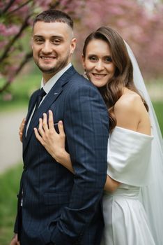 newlyweds walk in the park on the grass among cherry blossoms