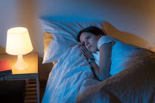 Beautiful girl suffering from insomnia lying in her bed looking through the window with Blue Colors from the moon. High quality photo