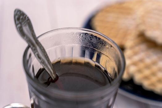 a glass of tea with a teaspoon close-up. sweet delicious creamy waffles sprinkled with powdered sugar. Breakfast by the window. Top view