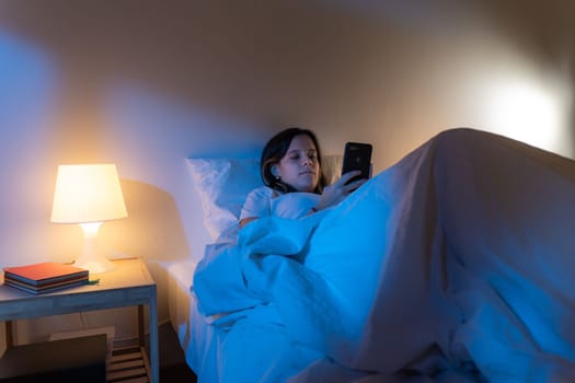 Girl looking her smart phone doom scrolling on bed in the middle of the night. Technology at bed concept. High quality photo