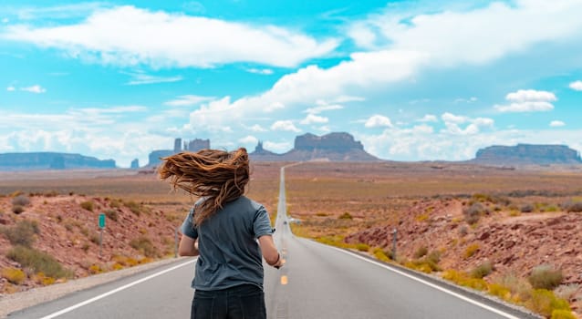 Attractive young woman from back view sitting in the middle of American straight road in the desert. High quality photo