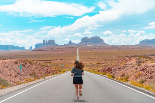Attractive young woman from back view sitting in the middle of American straight road in the desert. High quality photo