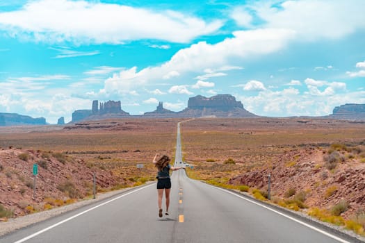 Attractive young woman from back view sitting in the middle of American straight road in the desert. High quality photo