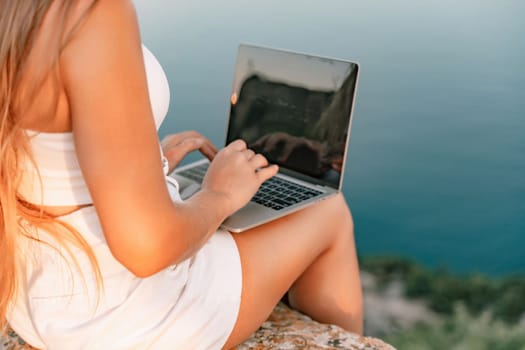 Freelance women sea working on the computer. Good looking middle aged woman typing on a laptop keyboard outdoors with a beautiful sea view. The concept of remote work