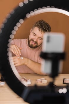 Man talking on cosmetics holding a makeup tools while recording his video. Guy making video for his blog on cosmetic product.