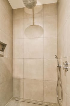 a shower room with beige tiles on the walls and floor, there is a hand held shower head in the corner