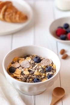 breakfast bowl of oat flakes with berries, yoghurt and croissant on the white wooden background, side view