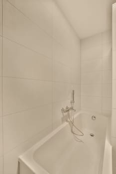 a bathroom with white tiles on the walls, and a shower head in the corner of the bathtub is attached to the wall