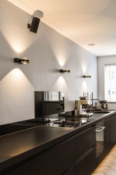 a modern kitchen with wood flooring and black countertops on the island in front of the sink is illuminated by two wall lights