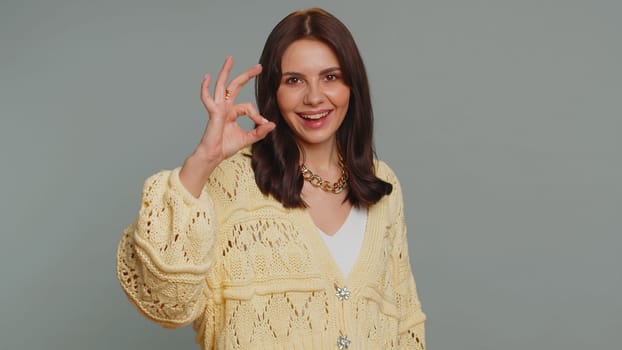 Ok. Joyful happy pretty woman in cardigan looking approvingly at camera showing approve feedback gesture like sign positive something good. Young girl on gray studio background. People sincere emotion