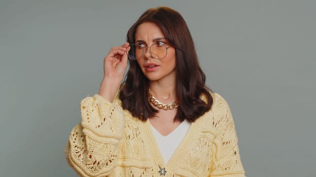 Exhausted tired pretty woman takes off glasses, feels eyes pain, being overwork burnout from long hours working, headache. Unhappy sad young adult girl isolated alone on gray studio background
