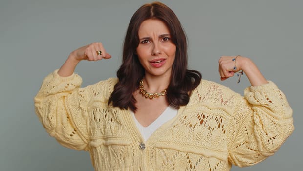 I am strong and independent. Proud success woman showing biceps and looking confident, feeling power strength to fight for rights energy to gain success win. Young adult girl on gray studio background
