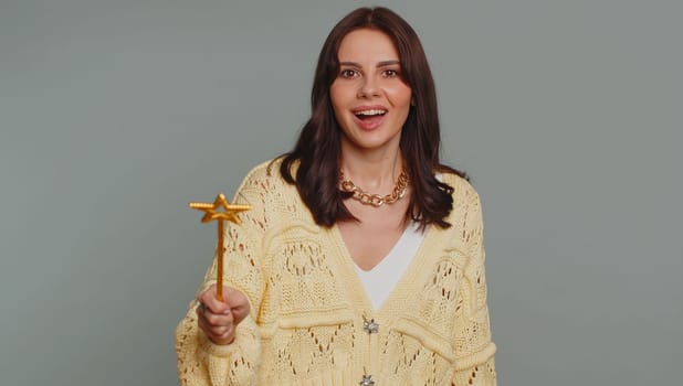Magician witch woman gesturing with magic wand fairy stick, making wish come true, casting magician spell, advertising holidays sale discount. Young pretty girl isolated on gray studio background