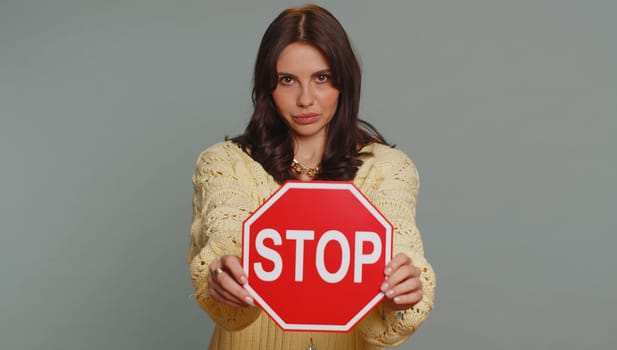 Serious pretty woman say No, hold inscription text red No stop danger sign, warning of finish, prohibited access declining communication, body language, trouble, protest. Girl on gray background