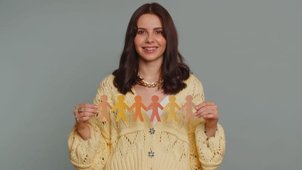 Woman showing multiracial different skin color human shape cut out of paper, concept of teamwork, partnership, community, unity, people support love, against racism. Young girl on gray background