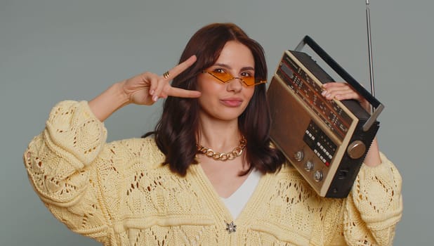 Happy woman in sunglasses using retro tape record player to listen music, disco dancing of favorite track, having fun, entertaining, fan of vintage technologies. Young girl isolated on gray background