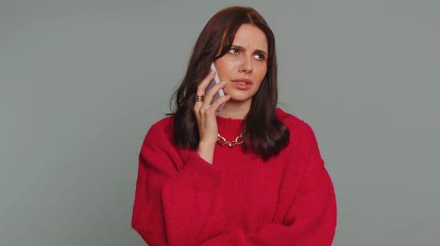 Lovely woman tired sleepy freelancer talking on mobile phone with friend, making online conversation. Disinterested sad young girl having annoyed boring talk on smartphone on gray studio background