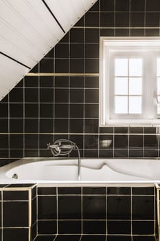 a bathroom with black tiles and white trim around the tub, window, and fauced bathtub on the wall
