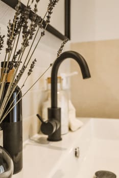 some flowers in a vase on a bathroom sink with soap and toothbrushs next to the faucet