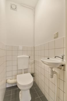 a white bathroom with black tile flooring and gray tiles on the walls, along with a toilet in the corner