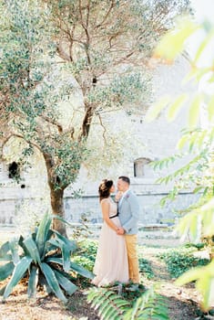 Bride and groom stand holding hands in the garden near the old fortress. High quality photo