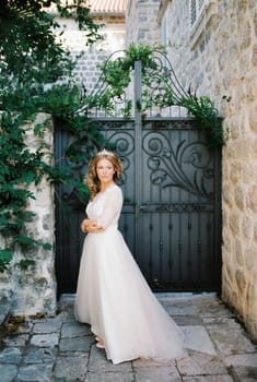 Bride in a white dress with a diadem stands in the courtyard of an old stone house. High quality photo