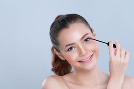 Closeup woman with blond hair putting glamorous black mascara with brush in hand on long thick eyelash. Perfect soft natural cosmetic makeup clean facial skin young woman in isolated background.