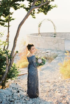 Bride with a bouquet stands on a mountain near an observation deck with a wedding arch. High quality photo