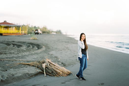 Smiling young woman standing on the beach near a pile of dry reeds. High quality photo