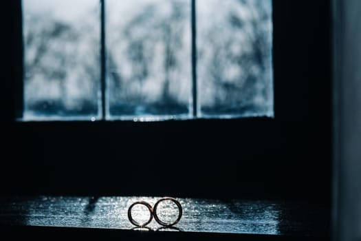 two gold wedding rings on the windowsill in the sunlight.