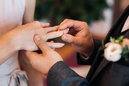 The groom puts an engagement ring on the bride's finger on their wedding day.