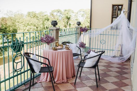 Delicate morning tea table setting with lilac flowers in Nesvizh castle, antique spoons and dishes on the table with a pink tablecloth.